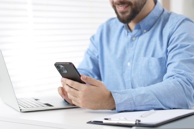 Young man using smartphone at white table in office, closeup