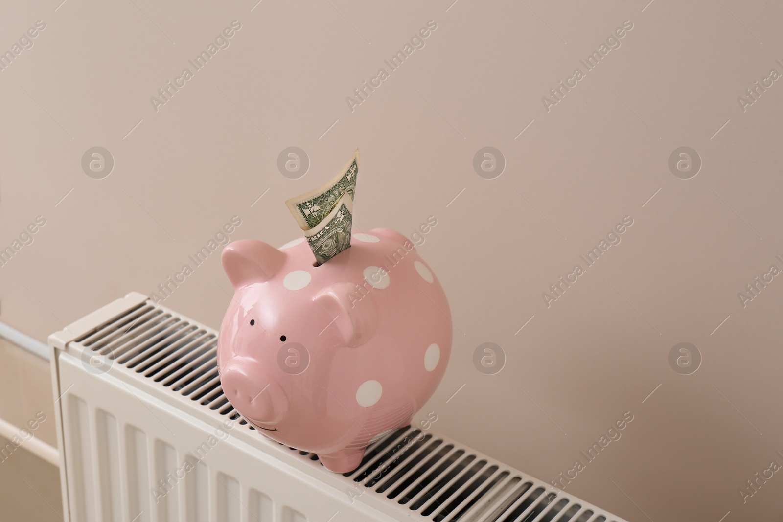 Photo of Heating radiator with piggy bank and money on color wall