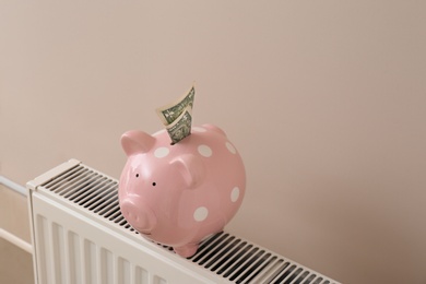 Photo of Heating radiator with piggy bank and money on color wall