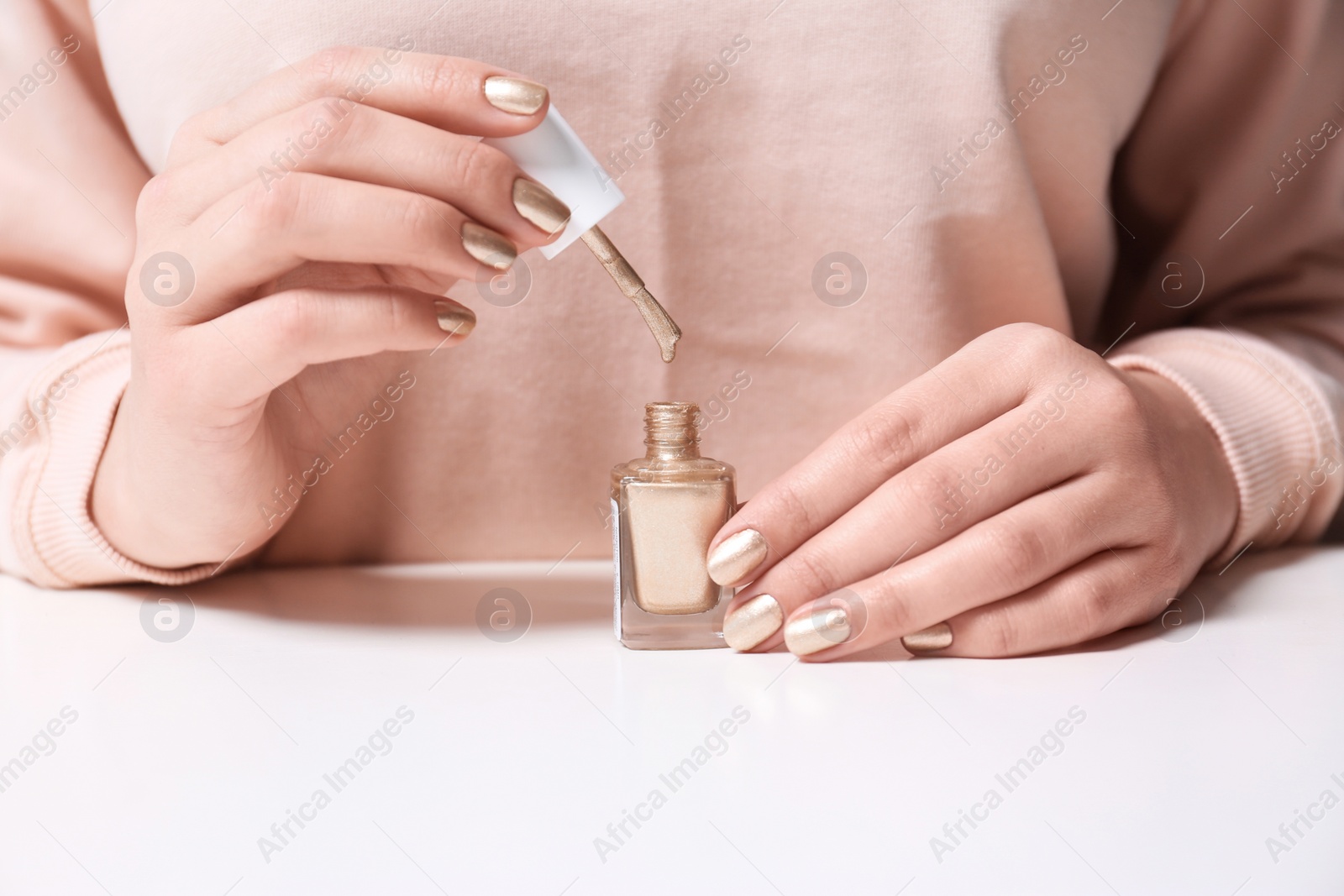 Photo of Woman with bottle of nail polish at table, closeup