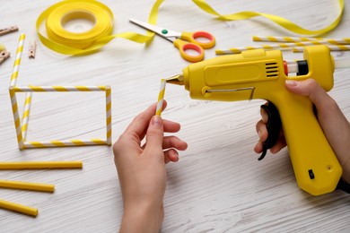 Photo of Woman with hot glue gun making craft at white wooden table, closeup