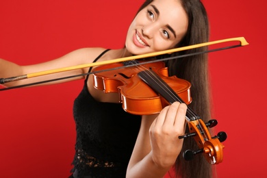 Beautiful woman playing violin on red background, focus on hand