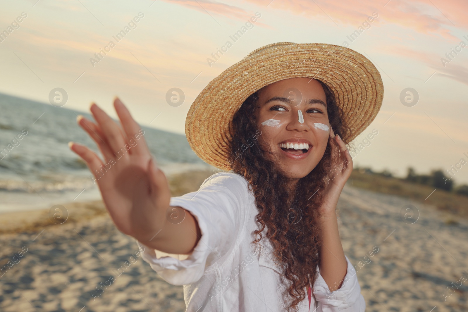 Photo of Happy African American woman with sun protection cream on face at beach