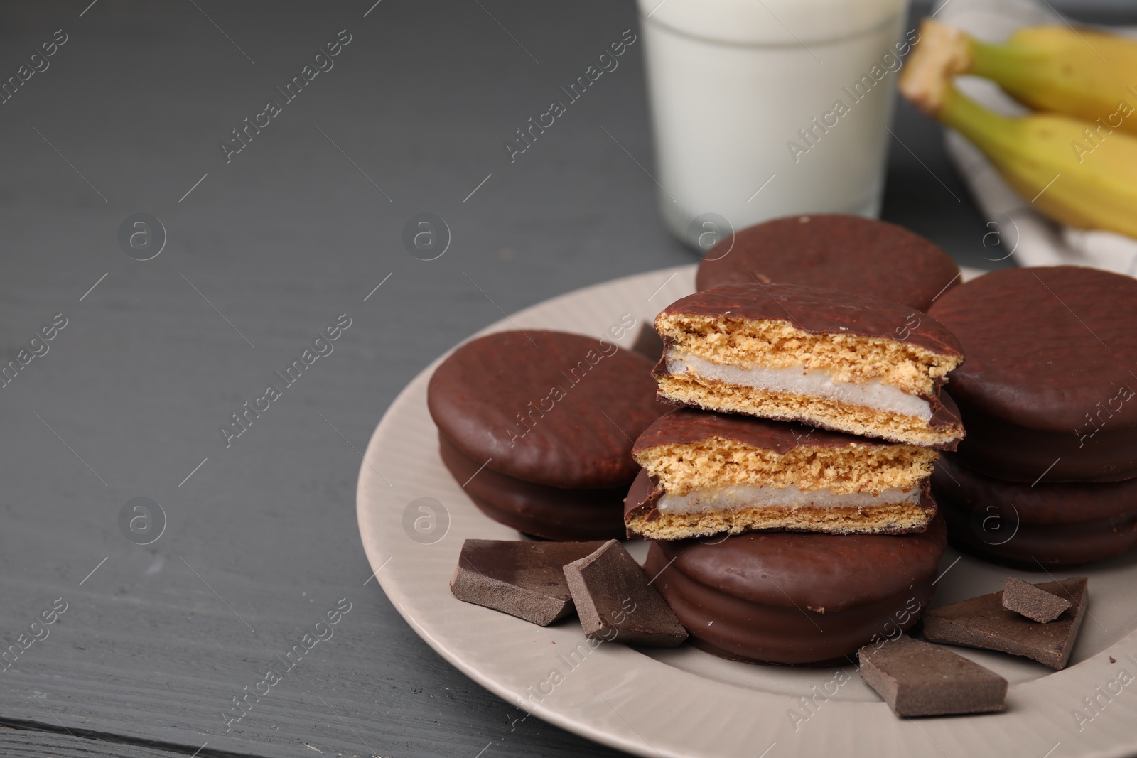 Photo of Tasty banana choco pies and pieces of chocolate on grey wooden table, closeup. Space for text