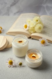 Burning scented candles and chamomile flowers on light gray textured table