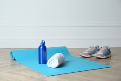 Exercise mat, towel, bottle of water and shoes on wooden floor indoors