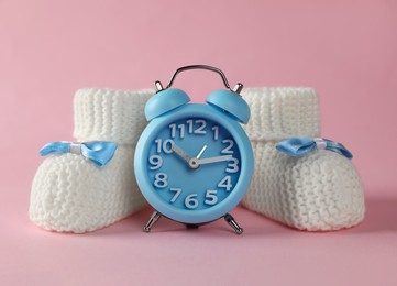 Photo of Alarm clock and baby booties on pink background. Time to give birth