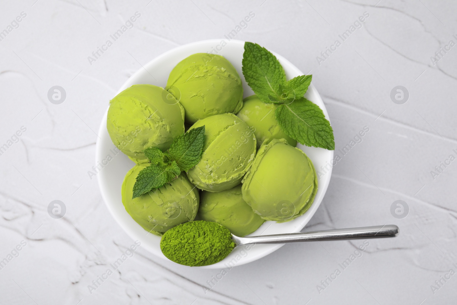 Photo of Tasty matcha ice cream and spoon with powder in bowl on white textured table, top view