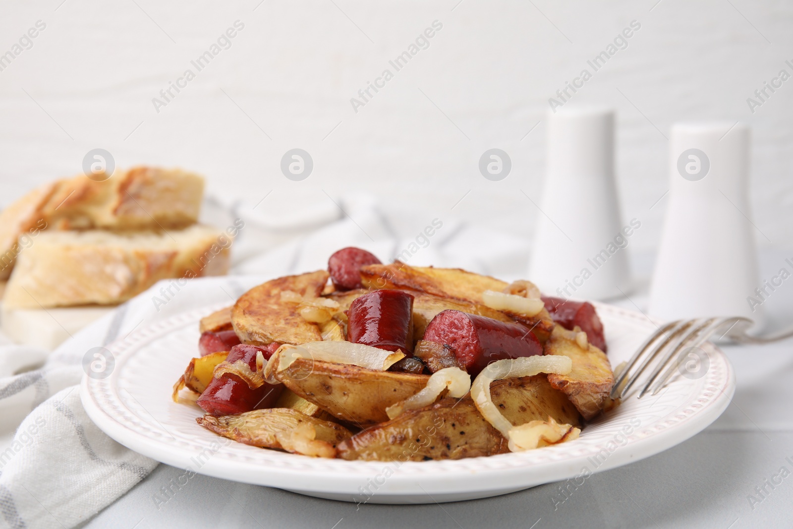 Photo of Delicious baked potato with thin dry smoked sausages and onion served on white table, closeup