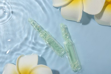 Photo of Skincare ampoules and beautiful plumeria flowers in water on light blue background, flat lay