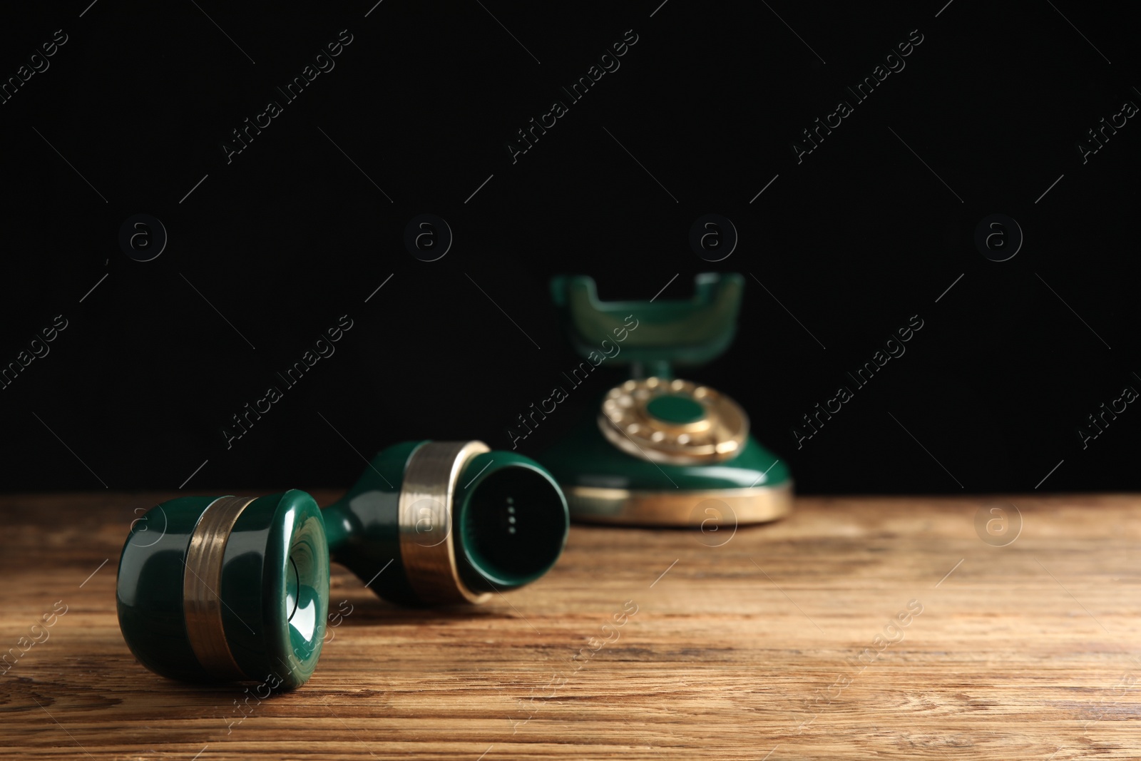 Photo of Handset of vintage corded phone on wooden table against black background, closeup
