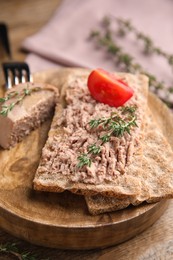 Photo of Crispy crackers with delicious meat pate and thyme served on wooden table, closeup