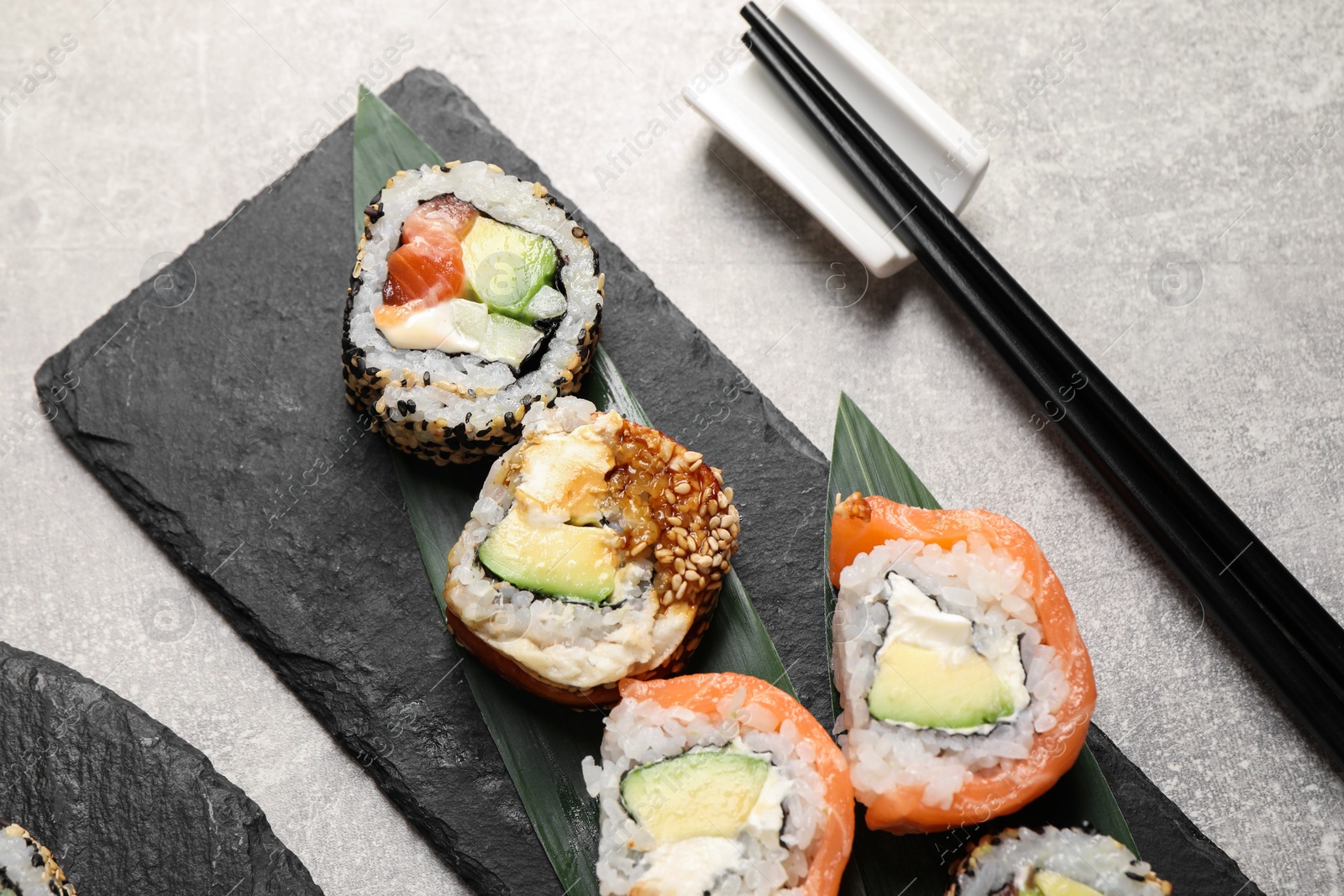 Photo of Delicious sushi rolls and chopsticks on light grey table, above view