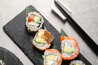 Delicious sushi rolls and chopsticks on light grey table, above view