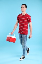 Man with cool box walking on light blue background
