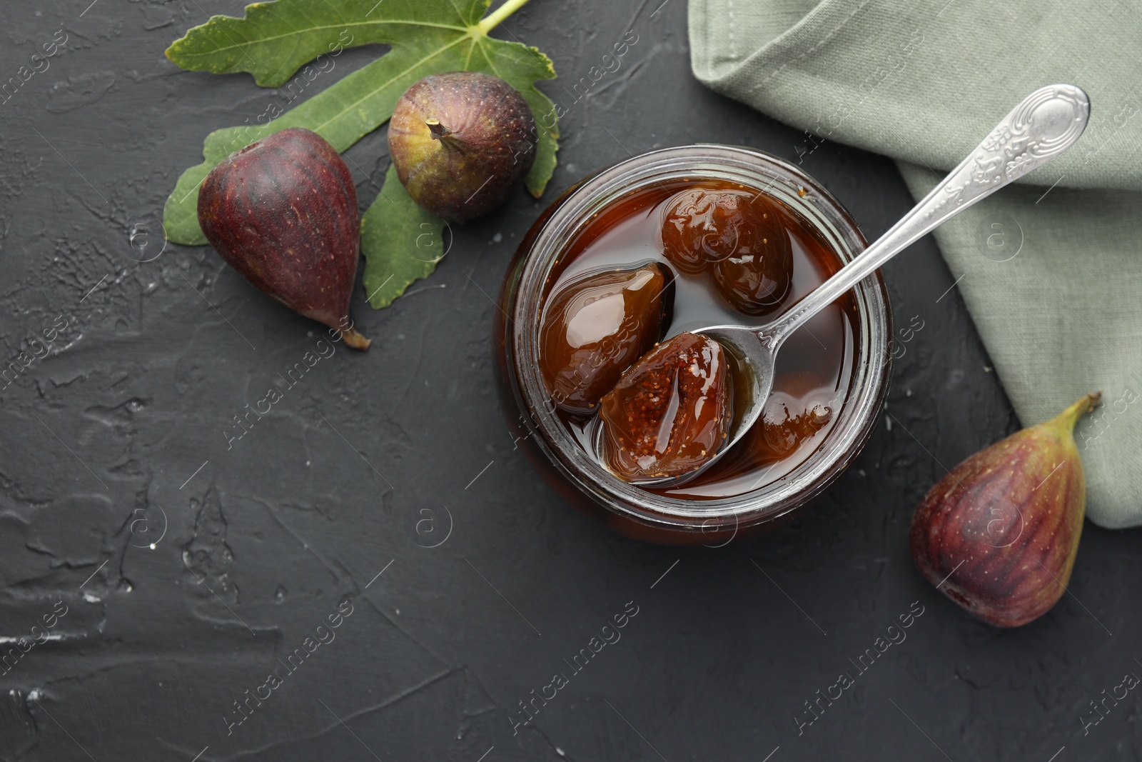 Photo of Jar of tasty sweet jam and fresh figs on black table, flat lay. Space for text