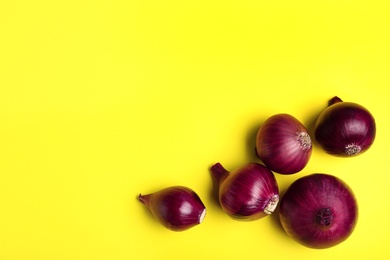 Photo of Whole red onion bulbs on yellow background, flat lay. Space for text