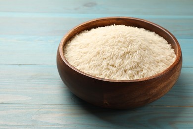 Photo of Raw basmati rice in bowl on light blue wooden table