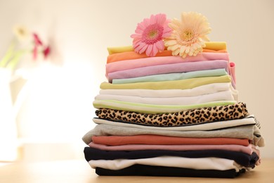 Photo of Stack of clean clothes and flowers on wooden table. Space for text