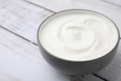 Delicious natural yogurt in bowl on light wooden table, closeup