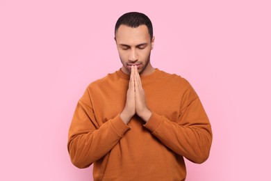 Photo of African American man with clasped hands praying to God on pink background