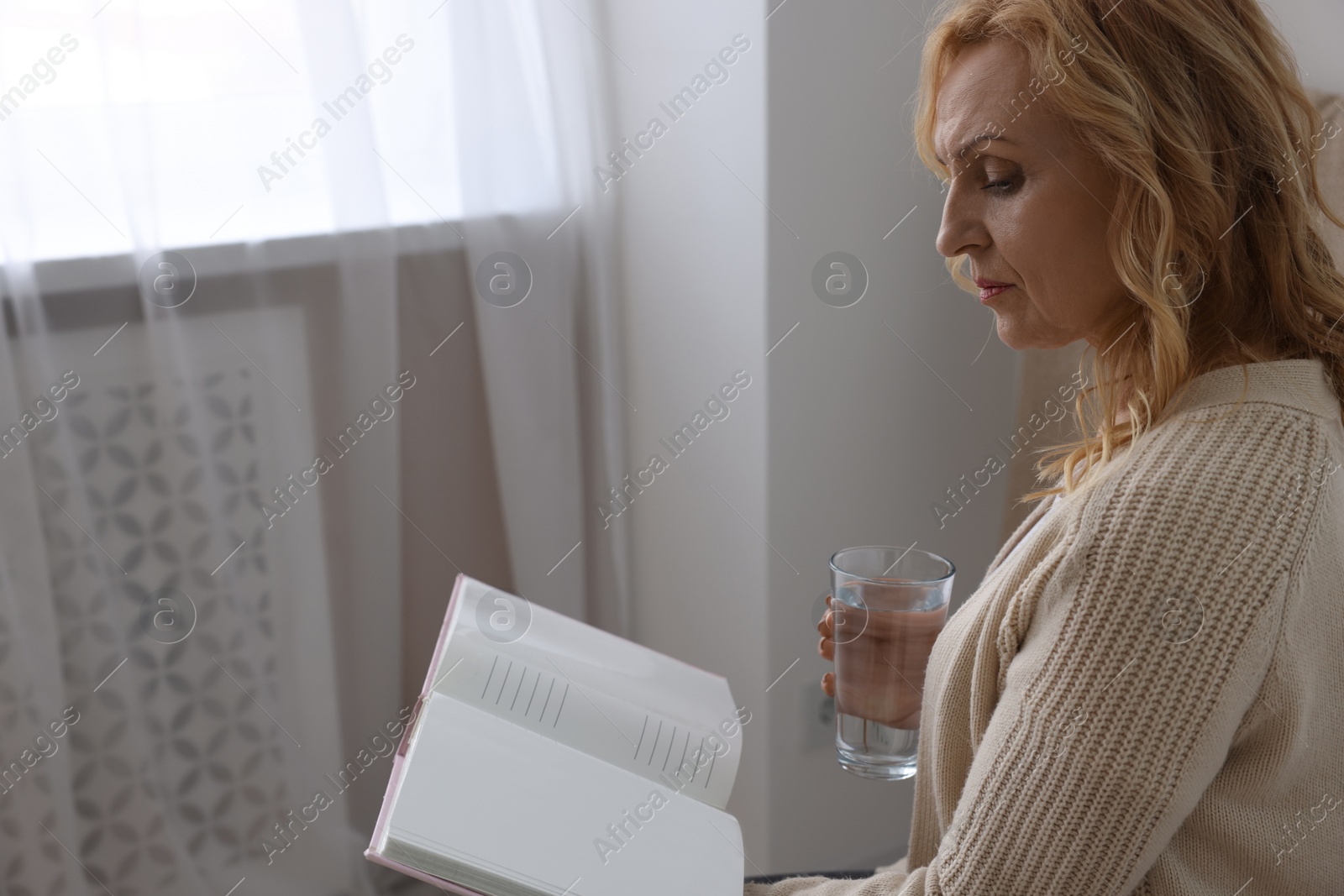 Photo of Upset middle aged woman with book and glass of water at home. Loneliness concept