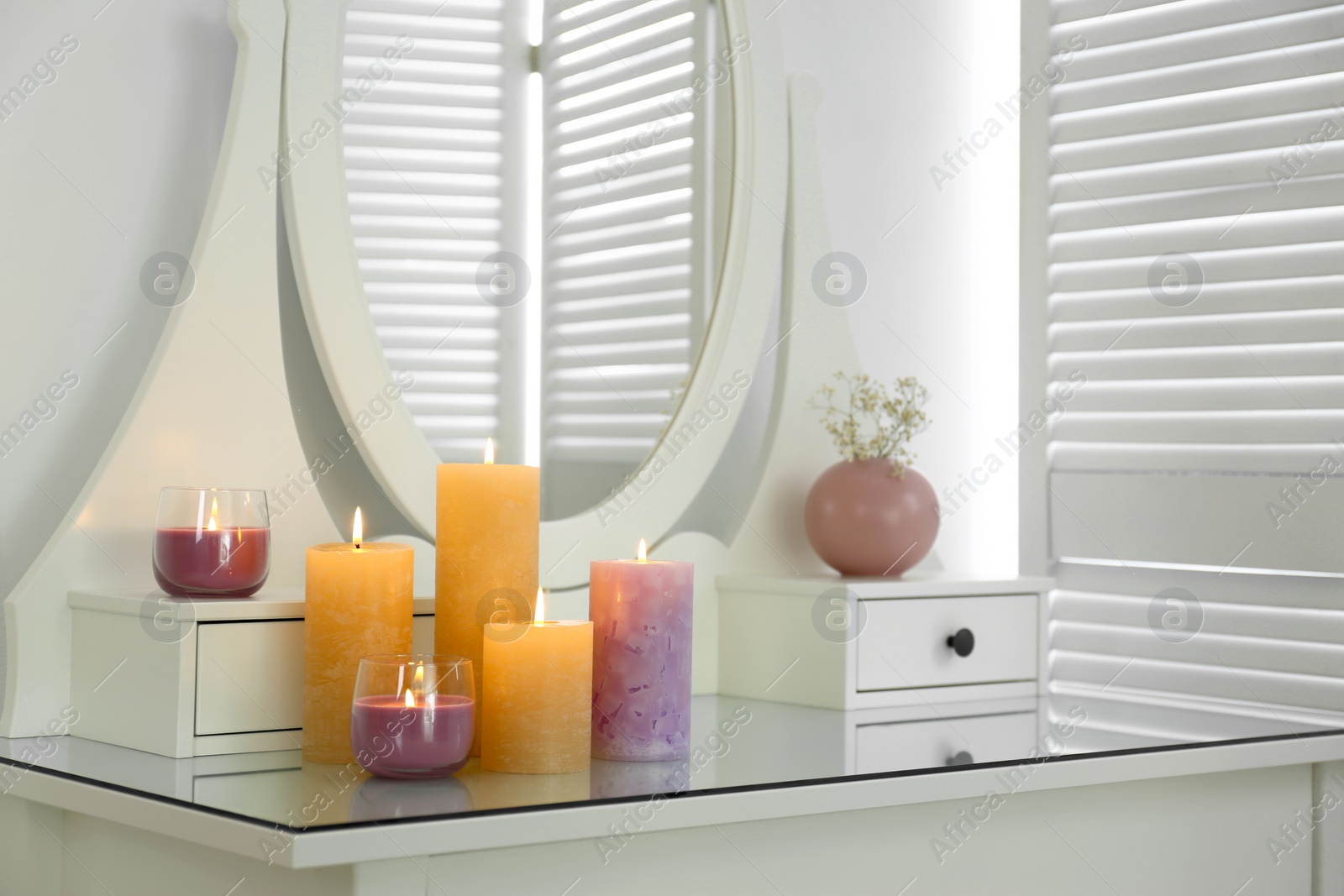 Photo of Different burning candles on dressing table in room
