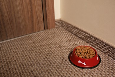 Dry dog food in feeding bowl on soft carpet indoors. Space for text