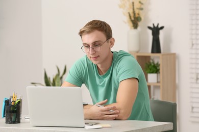 Photo of Young man with laptop at table indoors