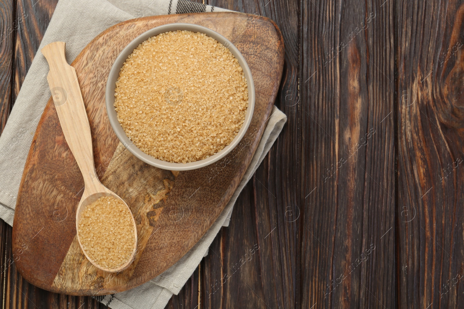 Photo of Brown sugar in bowl and spoon on wooden table, flat lay. Space for text