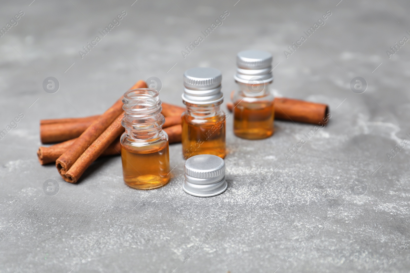 Photo of Bottles with cinnamon oil and sticks on grey background