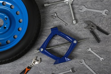 Photo of Car wheel, scissor jack and different tools on grey surface, flat lay