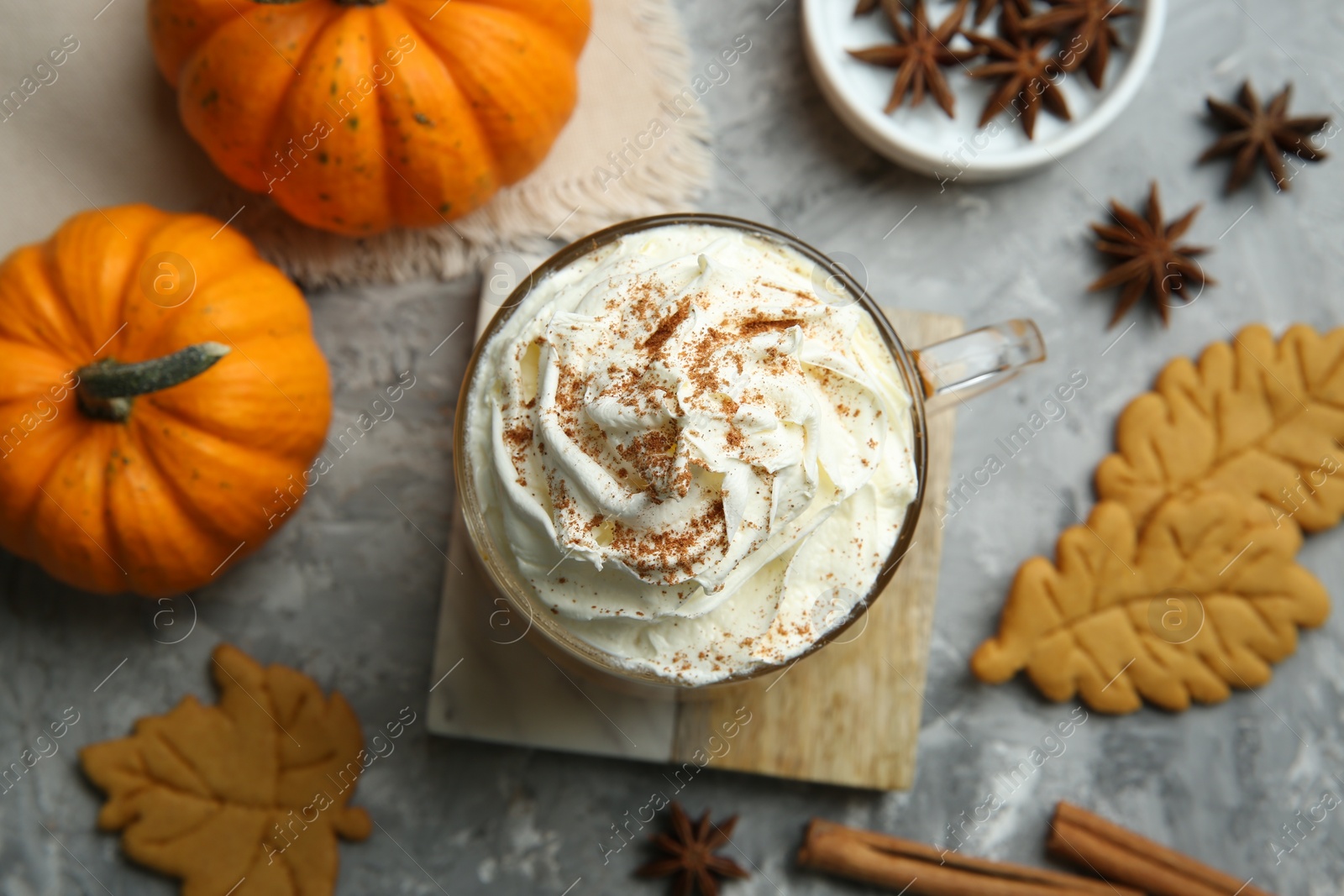 Photo of Cup of pumpkin spice latte with whipped cream, cookies and ingredients on light grey table, flat lay