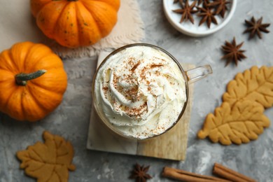 Photo of Cup of pumpkin spice latte with whipped cream, cookies and ingredients on light grey table, flat lay