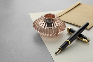 Photo of Stylish fountain pen, inkwell, envelope and paper on grey textured table, space for text