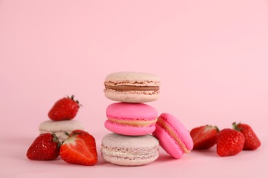 Delicious macarons and fresh strawberries on pink background, space for text