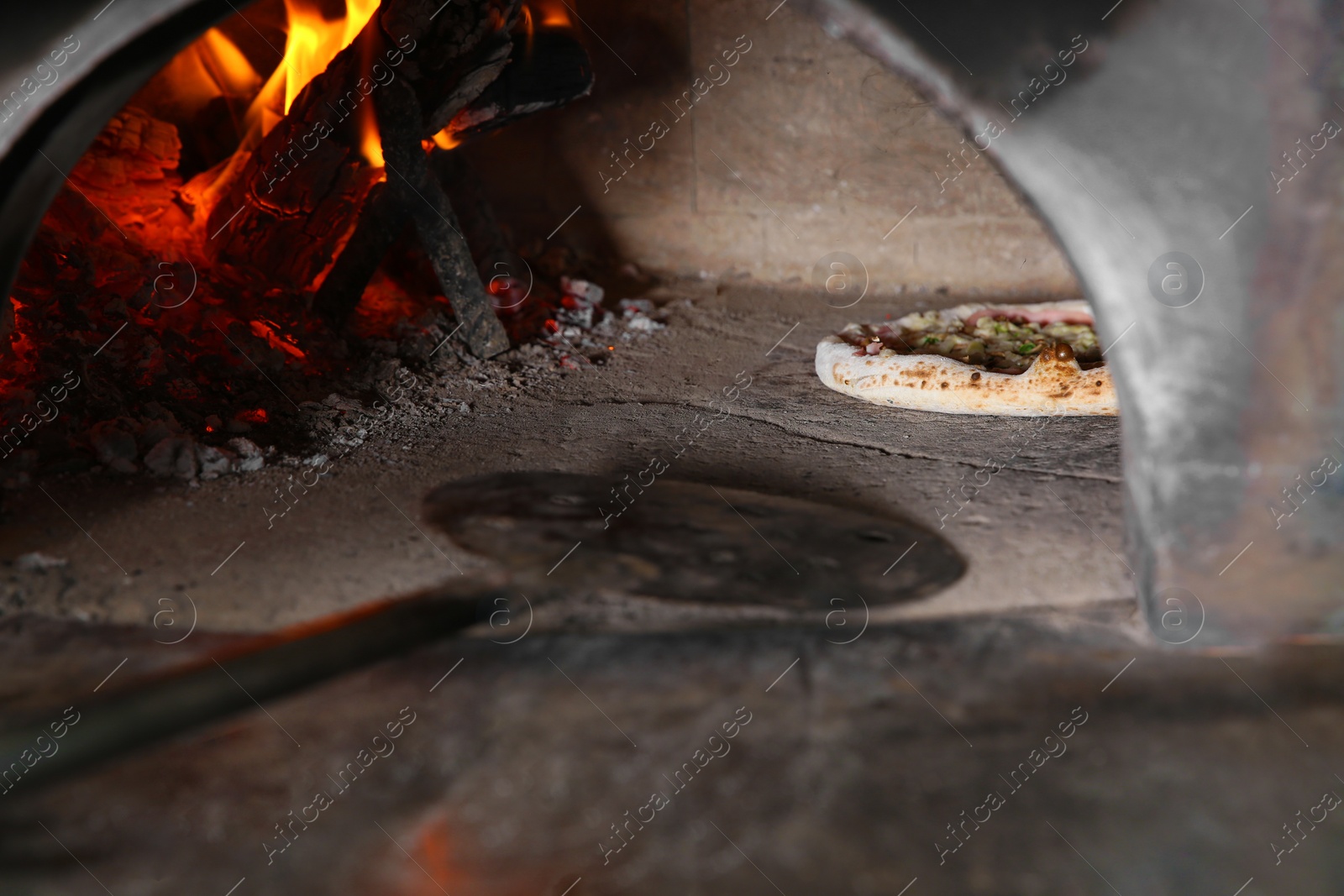 Photo of Burning firewood and tasty pizza in oven at restaurant kitchen