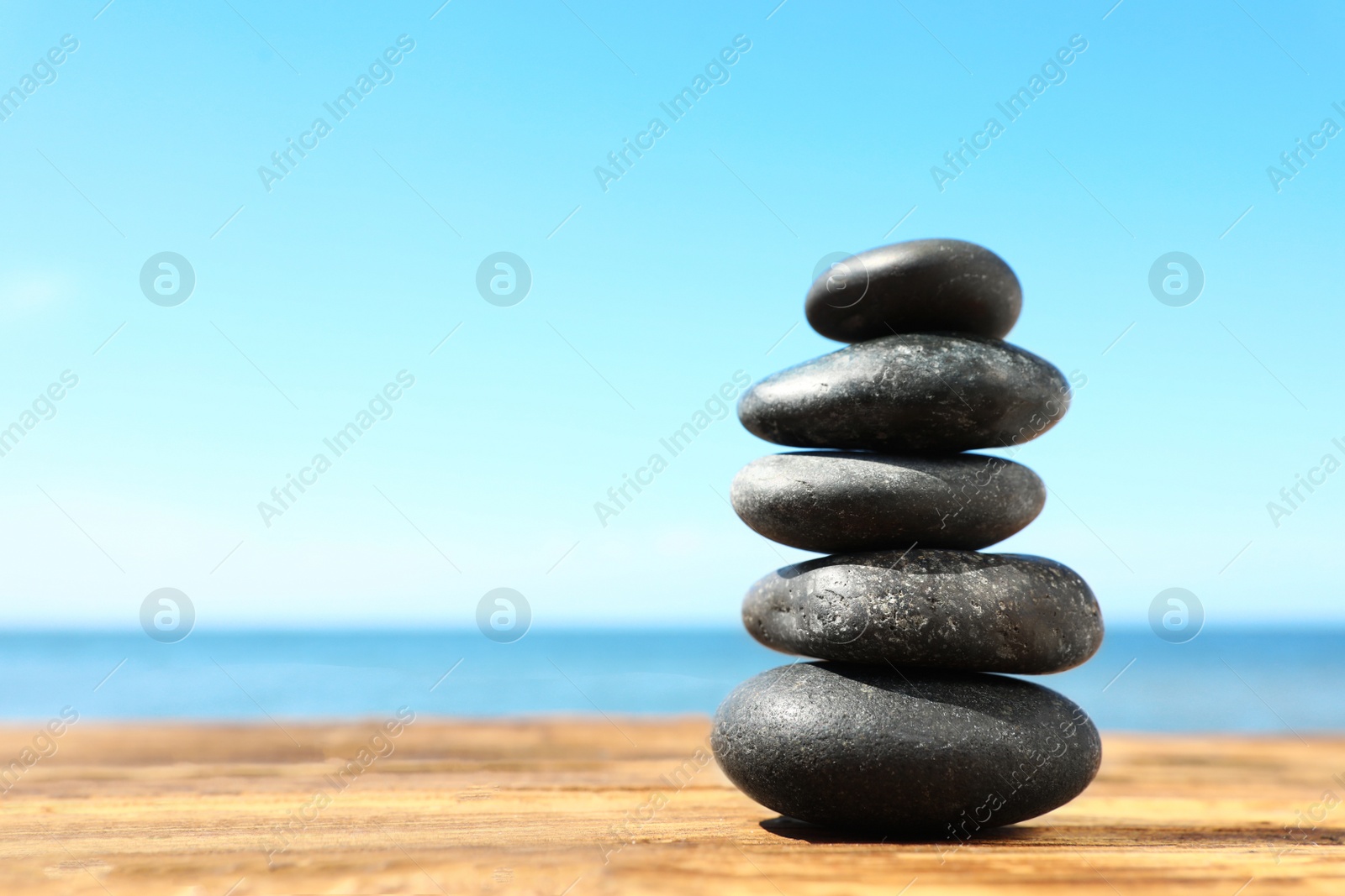 Photo of Stack of stones on wooden table against seascape, space for text. Zen concept