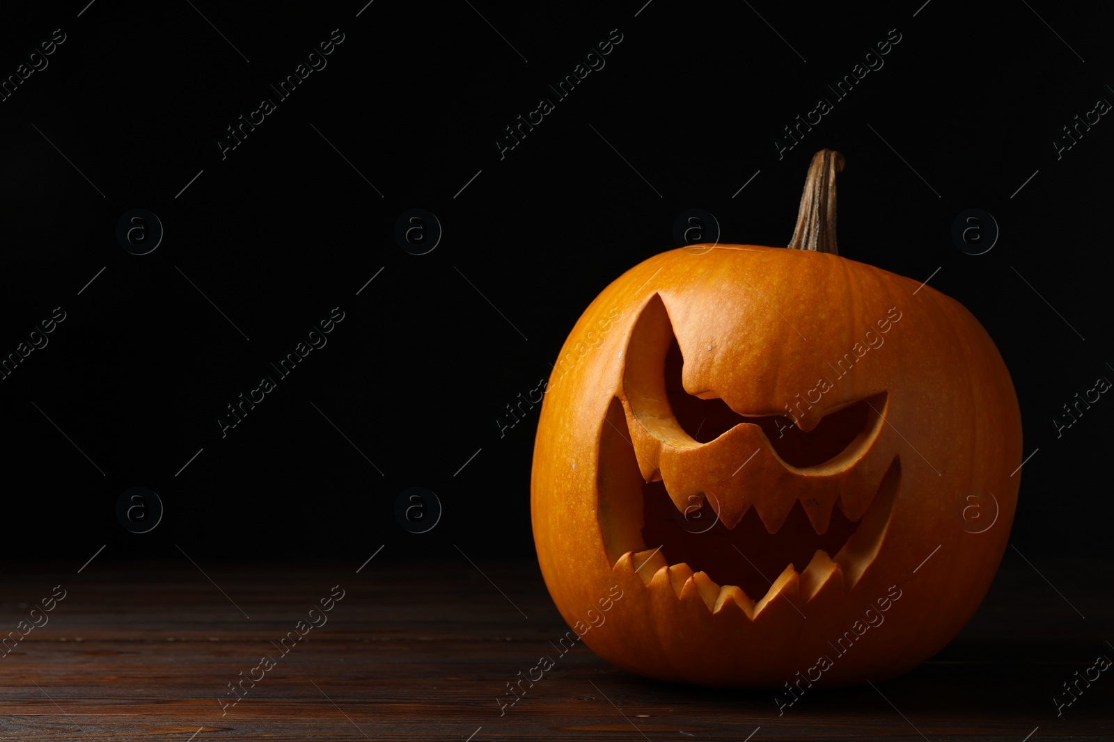Photo of Scary jack o'lantern made of pumpkin on wooden table in darkness, space for text. Halloween traditional decor