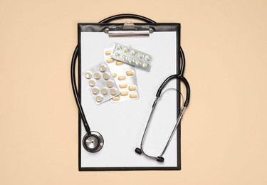 Stethoscope, pills and clipboard on beige background, top view. Medical tool