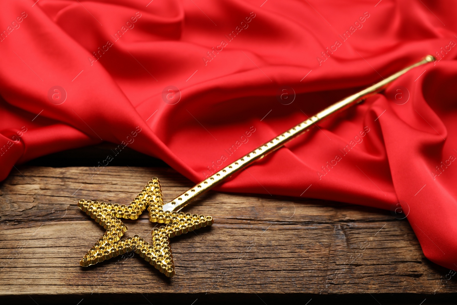 Photo of Beautiful golden magic wand and red fabric on wooden table