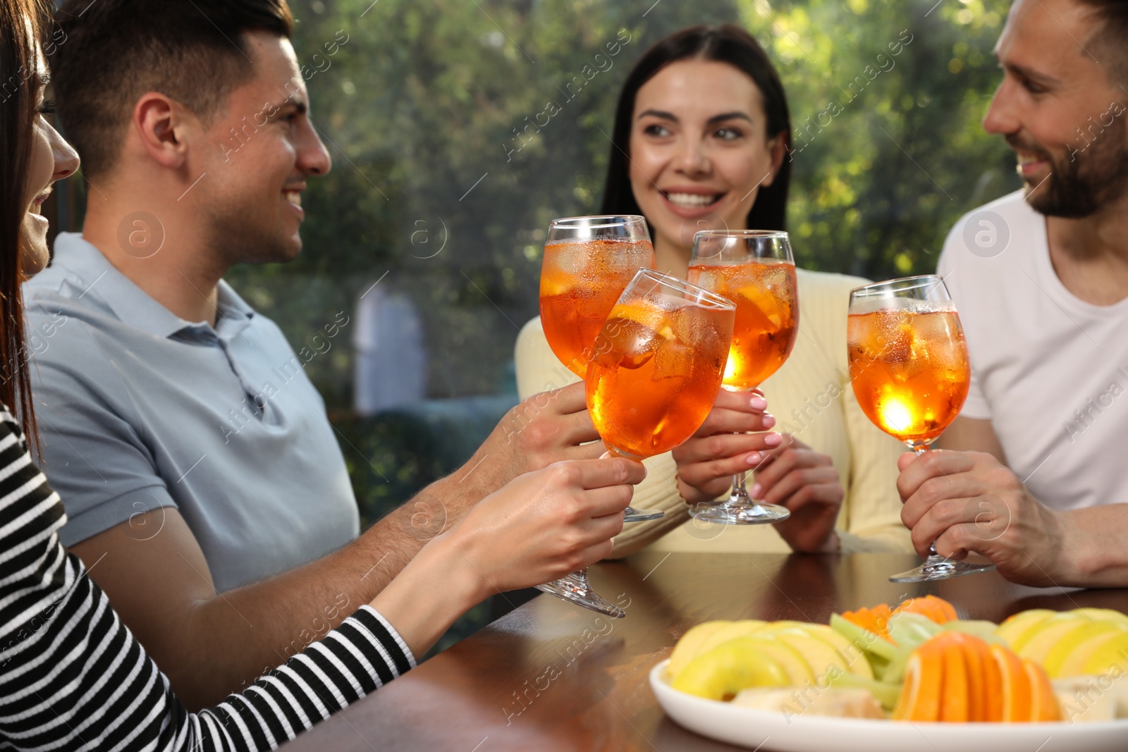 Photo of Friends clinking glasses of Aperol spritz cocktails at table