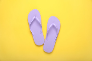Photo of Stylish violet flip flops on yellow background, top view