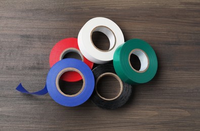 Photo of Colorful insulating tapes on wooden table, flat lay