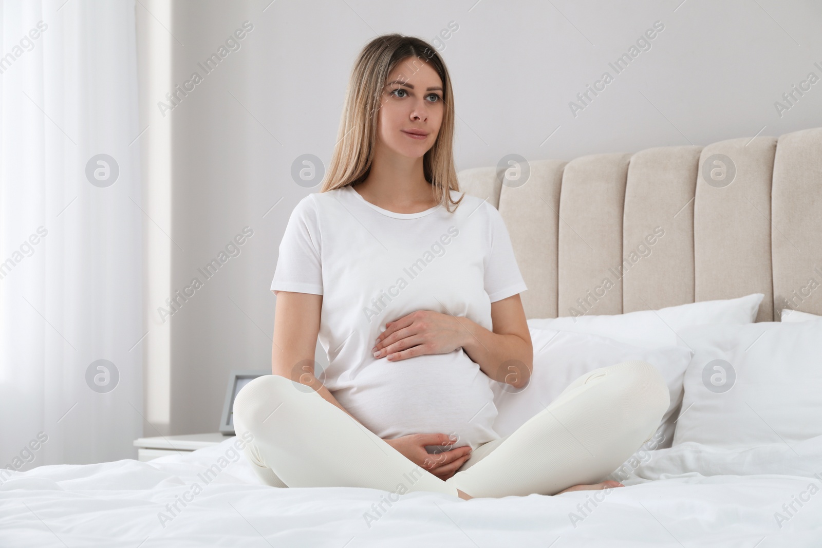 Photo of Beautiful pregnant woman sitting on bed at home