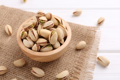 Tasty pistachios in bowl on white wooden table, space for text