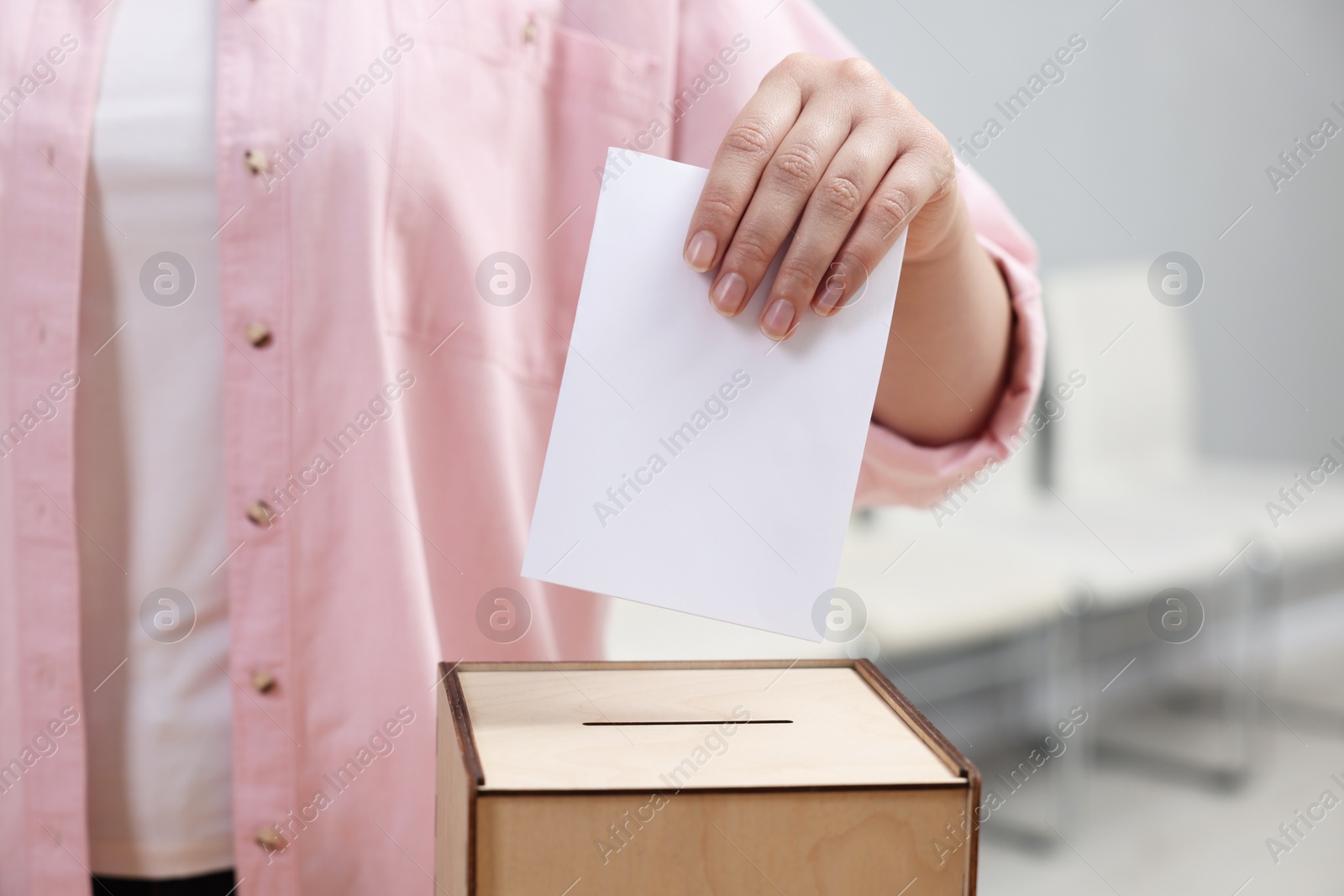 Photo of Woman putting her vote into ballot box on blurred background, closeup