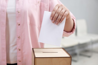 Photo of Woman putting her vote into ballot box on blurred background, closeup