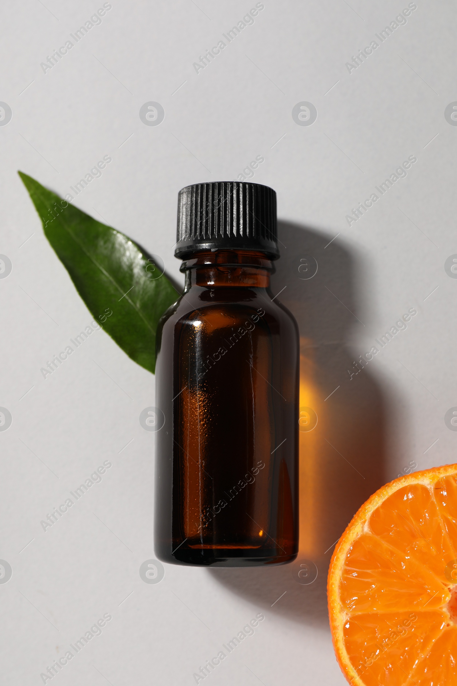 Photo of Aromatic tangerine essential oil in bottle, leaf and citrus fruit on grey table, top view