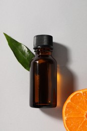 Photo of Aromatic tangerine essential oil in bottle, leaf and citrus fruit on grey table, top view